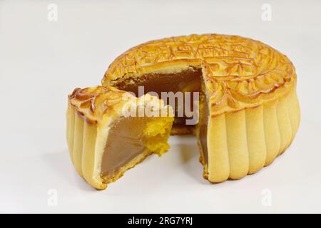 Una torta lunare cinese al forno con pasta di semi di loto e un cuneo di un quarto di taglio contenente tuorlo d'uovo d'anatra salato, su bianco Foto Stock