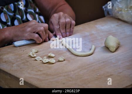 Primo piano sulle mani di una donna che prepara le orecchiette, la tipica pasta pugliese, sulla strada del centro di Bari Foto Stock