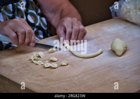 Primo piano sulle mani di una donna che prepara le orecchiette, la tipica pasta pugliese, sulla strada del centro di Bari Foto Stock