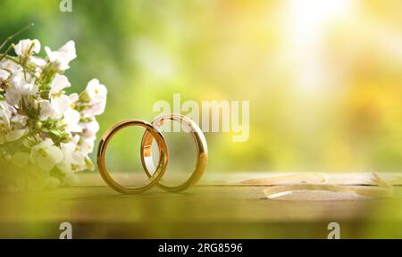 Dettaglio di due anelli d'oro su un tavolo rustico in legno con bouquet di fiori all'esterno con sfondo naturale. Vista frontale. Foto Stock