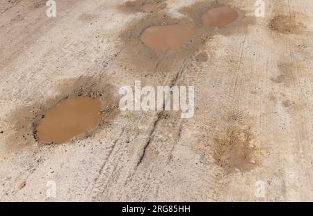 una strada sterrata con un sacco di buchi d'acqua, pozzanghere su una strada sterrata dopo piogge Foto Stock