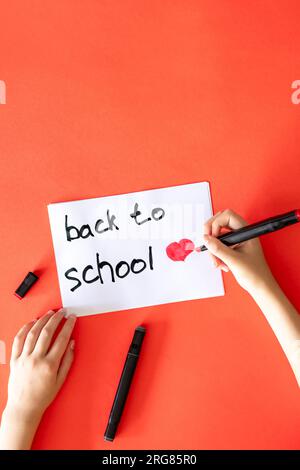 Tornando a scuola la mano del bambino scrive su un giornale su sfondo rosso. Foto Stock