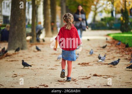 Adorabile bambina in età prescolare che si gode una bella e soleggiata giornata autunnale all'aperto. Felice bambino a caccia di piccioni a Parigi, in Francia. Attività autunnali all'aperto per bambini Foto Stock