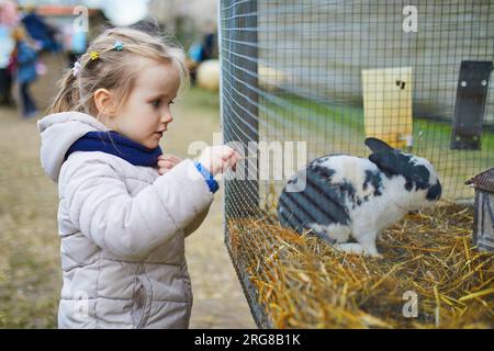 Adorabile bambina che dà da mangiare al coniglio alla fattoria. Bambino che si familiarizza con gli animali. Agricoltura e giardinaggio per bambini piccoli. Attività all'aperto per Foto Stock