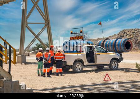 il team dirigenziale della miniera di diamanti parla dei piani di lavoro dietro un veicolo 4x4 su una strada sterrata sotto un ponte Foto Stock