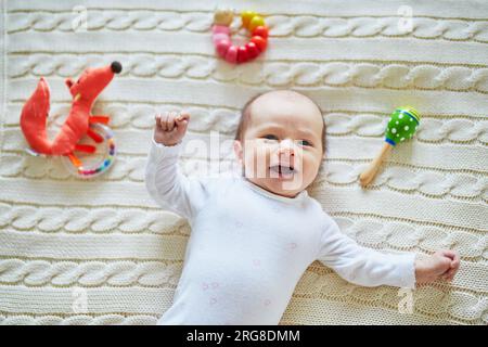 Neonata sdraiata su una coperta a maglia, sorridendo e guardando i colorati giocattoli a sonaglino di legno. bambino di un mese a casa Foto Stock