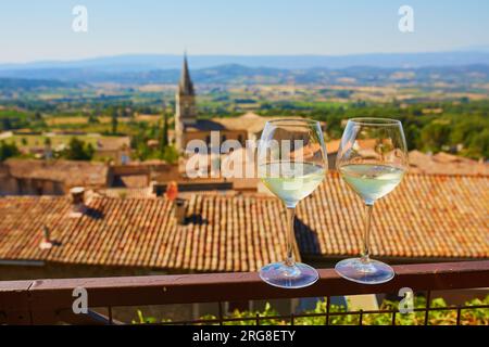 Due bicchieri di vino bianco con vista sui bei tetti antichi del villaggio di Bonnieux in Provenza, Francia Foto Stock