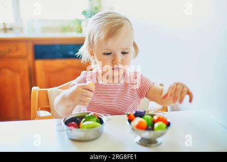 Adorabile bambina che gioca con frutta e verdura giocattolo a casa, all'asilo o all'asilo. Giochi creativi al coperto per bambini Foto Stock