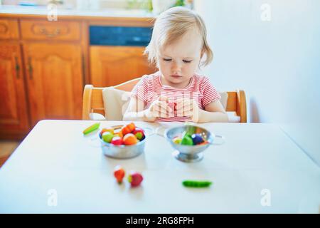 Adorabile bambina che gioca con frutta e verdura giocattolo a casa, all'asilo o all'asilo. Giochi creativi al coperto per bambini Foto Stock