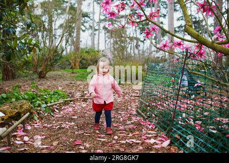 Adorabile bambina vicino alla gigantesca magnolia in piena fioritura. Bambini che esplorano la natura al Park Floral di Parigi, Francia Foto Stock