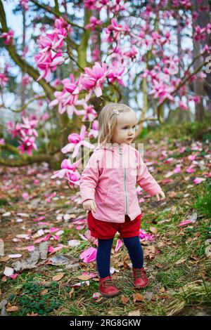 Adorabile bambina vicino alla gigantesca magnolia in piena fioritura. Bambini che esplorano la natura Foto Stock