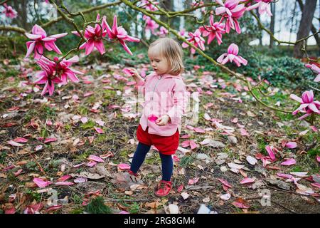 Adorabile bambina vicino alla gigantesca magnolia in piena fioritura. Bambini che esplorano la natura al Park Floral di Parigi, Francia Foto Stock