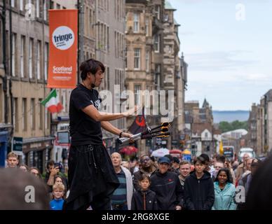 Uno Street performer che mangia il fuoco circondato dalla folla si esibisce sul Royal Mile di Edimburgo durante il festival Fringe, agosto 2023. Scozia, Regno Unito. Foto Stock