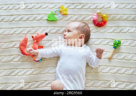 Neonata sdraiata su una coperta a maglia, sorridendo e guardando i colorati giocattoli a sonaglino di legno. bambino di un mese a casa Foto Stock