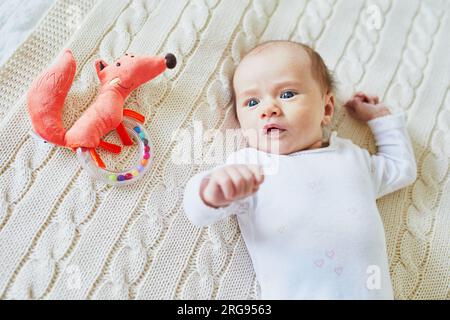 Neonata sdraiata su una coperta a maglia, sorridendo e guardando il colorato giocattolo di legno a sonaglino. bambino di un mese a casa Foto Stock