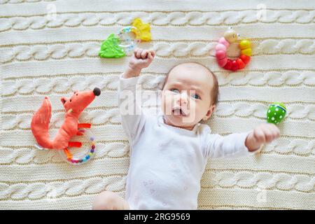 Neonata sdraiata su una coperta a maglia, sorridendo e guardando i colorati giocattoli a sonaglino di legno. bambino di un mese a casa Foto Stock