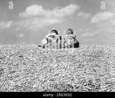 Coppia di mezza età contenta al mare, seduta in sdraio su una spiaggia di ciottoli con un cesto da picnic. Foto Stock