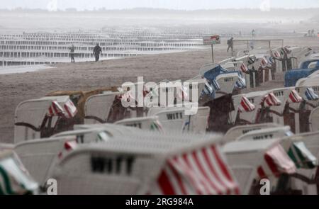 8 agosto 2023, Meclemburgo-Pomerania occidentale, Graal-Müritz: La spiaggia del Mar Baltico è quasi deserta, le sdraio sono in piedi sotto la pioggia. Venti forti e pioggia hanno allontanato i vacanzieri. Foto: Bernd Wüstneck/dpa Foto Stock