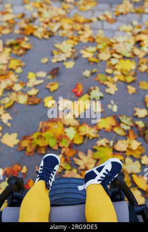 Bambina in abiti eleganti e luminosi seduta su una poltrona all'aperto in autunno. Passeggiate autunnali con i bambini Foto Stock