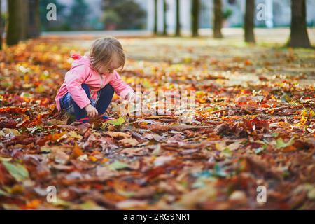 Adorabile bambina che raccoglie castagne nel giardino delle Tuileries a Parigi, in Francia. Un bambino felice che si gode la calda e soleggiata giornata autunnale. Attività autunnali all'aperto Foto Stock