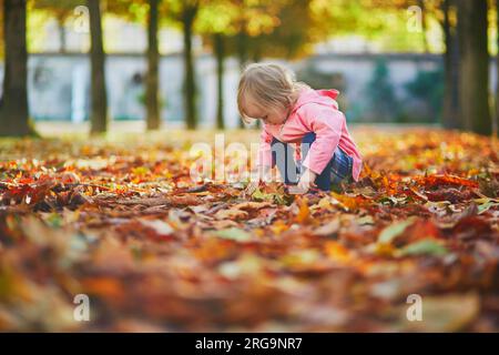 Adorabile bambina che raccoglie castagne nel giardino delle Tuileries a Parigi, in Francia. Un bambino felice che si gode la calda e soleggiata giornata autunnale. Attività autunnali all'aperto Foto Stock