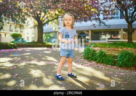 Allegra bambina di due anni che si diverte nel parco con i ciliegi in fiore a Parigi, in Francia Foto Stock