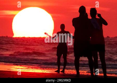 Isola di Palms, Stati Uniti. 8 agosto 2023. I turisti fanno selfie mentre il sole sorge sulla spiaggia in una giornata da record nella zona di Charleston, l'8 agosto 2023 a Isle of Palms, South Carolina. Un'ondata di caldo persistente in tutto il sud degli Stati Uniti continua a portare nella regione un clima estremamente caldo e umido. Crediti: Richard Ellis/Richard Ellis/Alamy Live News Foto Stock