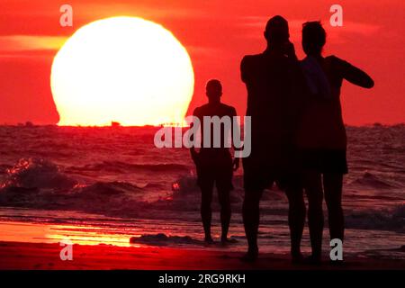 Isola di Palms, Stati Uniti. 8 agosto 2023. I turisti fanno selfie mentre il sole sorge sulla spiaggia in una giornata da record nella zona di Charleston, l'8 agosto 2023 a Isle of Palms, South Carolina. Un'ondata di caldo persistente in tutto il sud degli Stati Uniti continua a portare nella regione un clima estremamente caldo e umido. Crediti: Richard Ellis/Richard Ellis/Alamy Live News Foto Stock