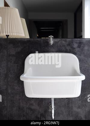Lavandino da bagno con supporto medico a parete bianco grande su decorazione murale in cemento nero vicino a grande specchio e lampada in piedi in bagno, ve Foto Stock