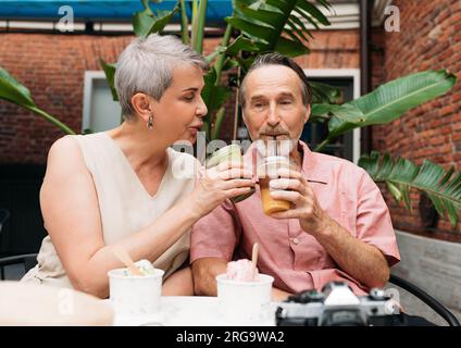 Coppia matura seduta in un caffè all'aperto e sorseggiando un cocktail Foto Stock