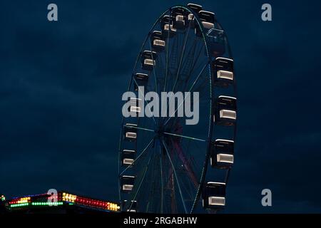moderna ruota panoramica con cabine chiuse al carnevale con cielo blu senza nuvole sullo sfondo ripresa ravvicinata con grandangolo illuminato Foto Stock