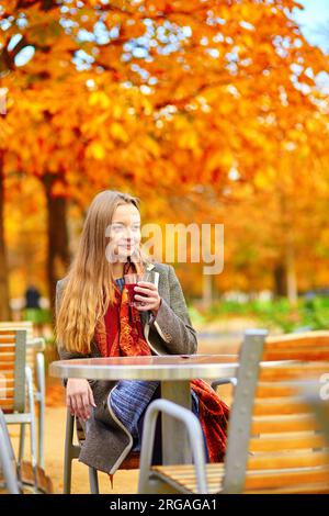 Bella giovane donna in un caffè di strada parigino che beve vino caldo in una splendida e colorata giornata autunnale Foto Stock