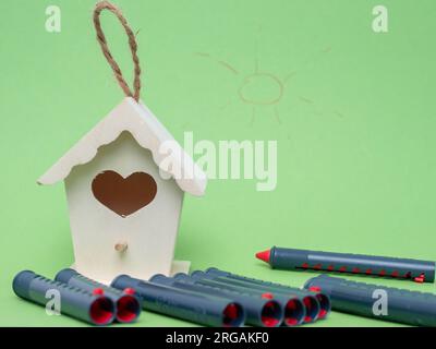 Casetta per uccelli e pastelli multicolore per disegnare su uno sfondo verde. Pastelli e birdhouse da vicino. Foto Stock