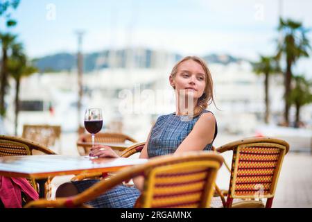 Giovane donna francese che beve vino rosso in un caffè all'aperto di Cannes Foto Stock