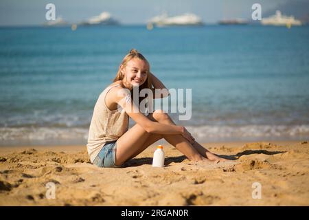 Bella giovane donna che applica la crema solare alle gambe Foto Stock