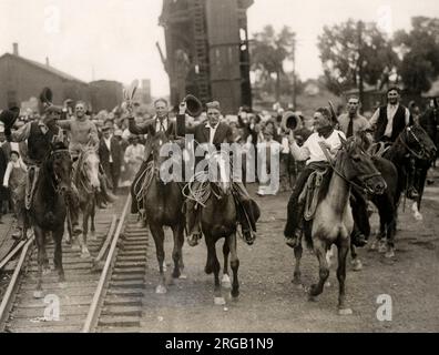 Nei primi anni del XX secolo vintage premere fotografia - rasserenante cowboy corsa lungo il binario ferroviario su cavalli, STATI UNITI D'AMERICA circa 1920s. Miglia città montana Foto Stock