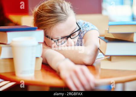 Bellissima giovane studentessa con molti libri, dormendo sul tavolo, stanca di prepararsi per gli esami. DOF poco profondo Foto Stock