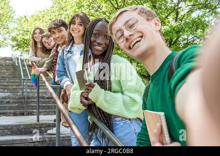 Diversi gruppi di studenti si riuniscono sulle scale del campus universitario, posando con zaini e oggetti di scena per gli studenti per un memorabile selfie di gruppo. Foto Stock