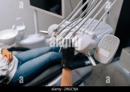 Vista ravvicinata di una stomatologa donna irriconoscibile in guanti che prende trapano elettrico dentale da un set di strumenti dentali per il trattamento del paziente Foto Stock