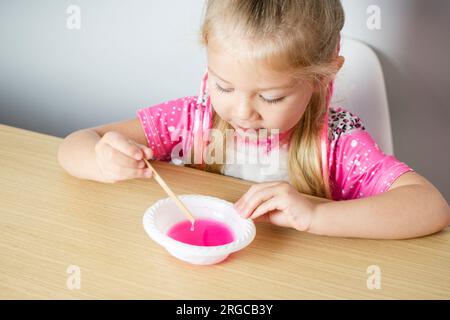 Carina ragazza caucasica sta facendo la melma da zero. Educazione dei bambini. A casa. Bambini che sperimentano. Foto Stock