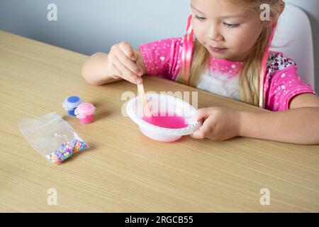 Carina ragazza caucasica sta facendo la melma da zero. Educazione dei bambini. A casa. Bambini che sperimentano. Foto Stock