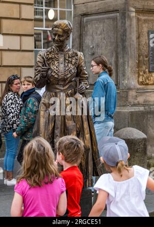 Royal Mile, Edimburgo, Scozia, Regno Unito, 8 agosto 2023. Artisti di strada di Edinburgh Fringe: Una statua vivente della scienziata Marie Curie intrattiene la folla di passaggio con i bambini che guardano. Crediti: Sally Anderson/Alamy Live News Foto Stock