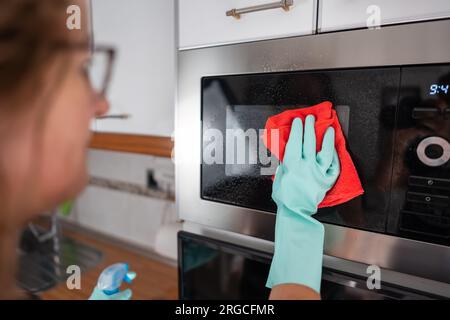 Donna che fa le pulizie in cucina mentre pulisce il forno a microonde. Foto Stock