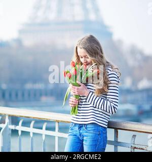 Bellissima ragazza con un mucchio di tulipani rossi vicino alla Torre Eiffel a Parigi, in Francia, in una chiara giornata primaverile Foto Stock