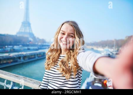 Bellissima ragazza che scatta divertenti selfie con il suo cellulare vicino alla Torre Eiffel Foto Stock