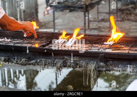 Grandi fiamme luminose prodotte dalle candele bruciate, cera di candela fusa che gocciola dal vassoio di metallo mentre le persone le posizionano e le posizionano con attenzione mentre pregano Gesù Foto Stock