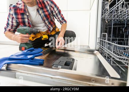 Addetto alla manutenzione che ripara la lavastoviglie in una cucina moderna. Concetto di manutenzione e assistenza domestica Foto Stock