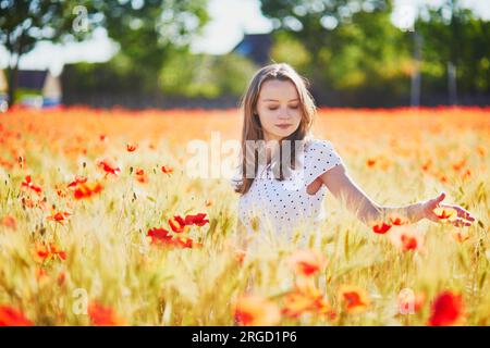 Giovane donna in abito bianco che cammina in un campo di papavero in un giorno d'estate. Ragazza che si gode i fiori in campagna Foto Stock