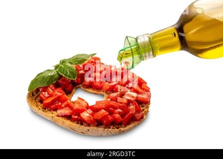 Friselle di pane italiano secco con pomodori ciliegini tritati e foglie di basilico condite con olio d'oliva versato dalla bottiglia d'olio - isolato su bianco e clippin Foto Stock