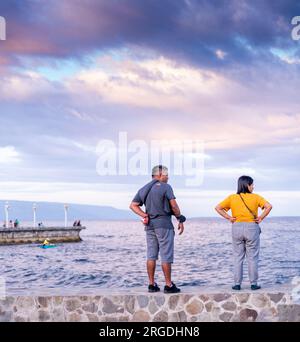 Dumaguete, Isola di Negros, Filippine - 1 febbraio 2023: Una coppia di mezza età filippina, guarda il mare e le barche che passano, mentre il muro si affaccia su un tranquillo panorama Foto Stock